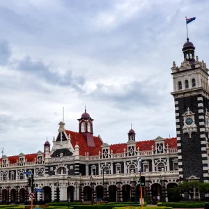 Fachada de la estación de tren de Dunedin, de piedra clara y tejado rojo, con su torre del reloj