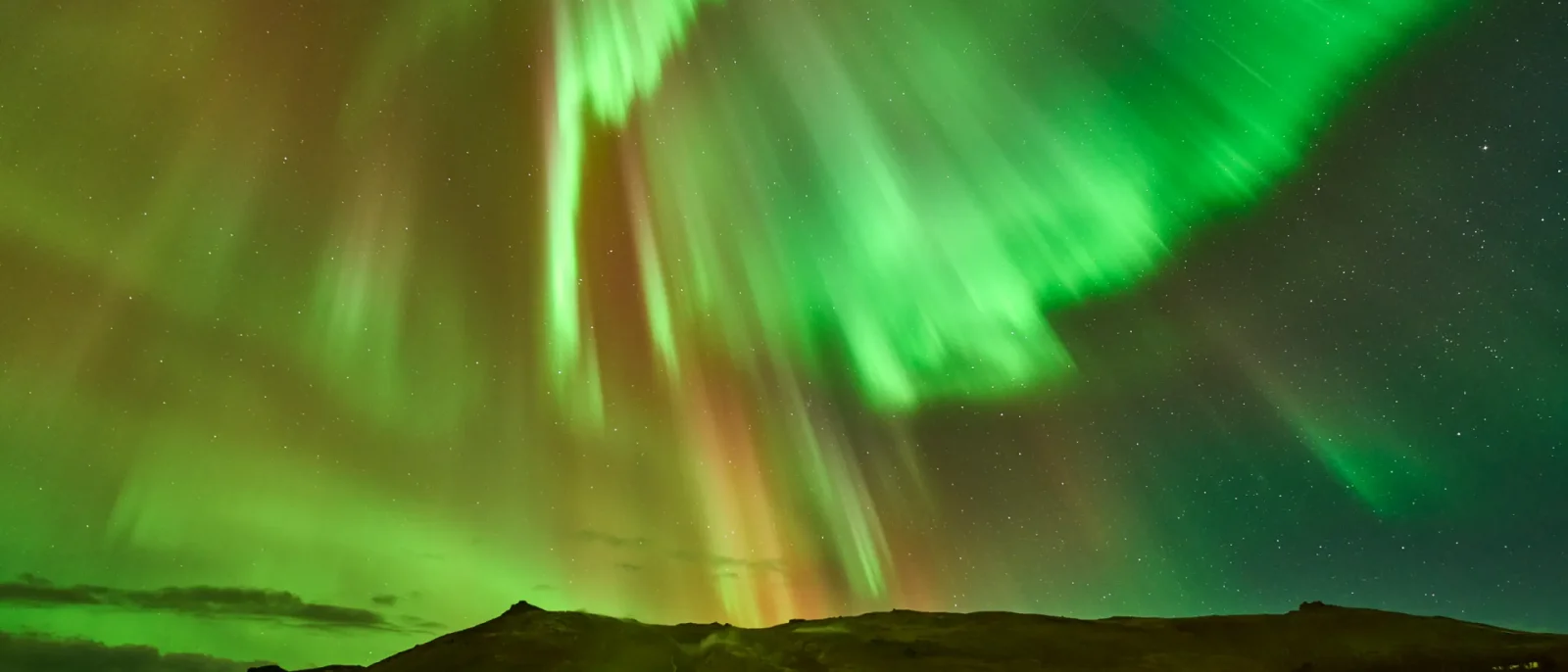 Aurora boreal verde iluminando el cielo nocturno sobre un paisaje salvaje de Islandia