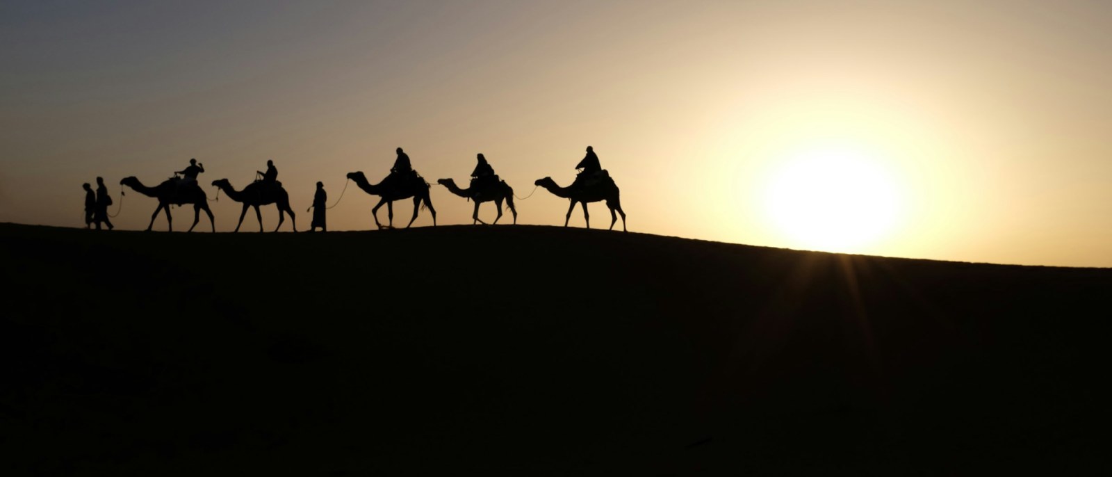 Silueta de un grupo montando camellos al atardecer entre las dunas del Sahara, en Merzouga.