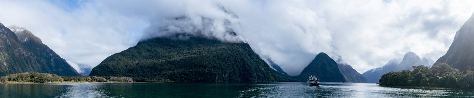 Mitre Peak reflejado en las aguas tranquilas del fiordo de Milford Sound, en la Isla Sur de Nueva Zelanda, con montañas entre la niebla