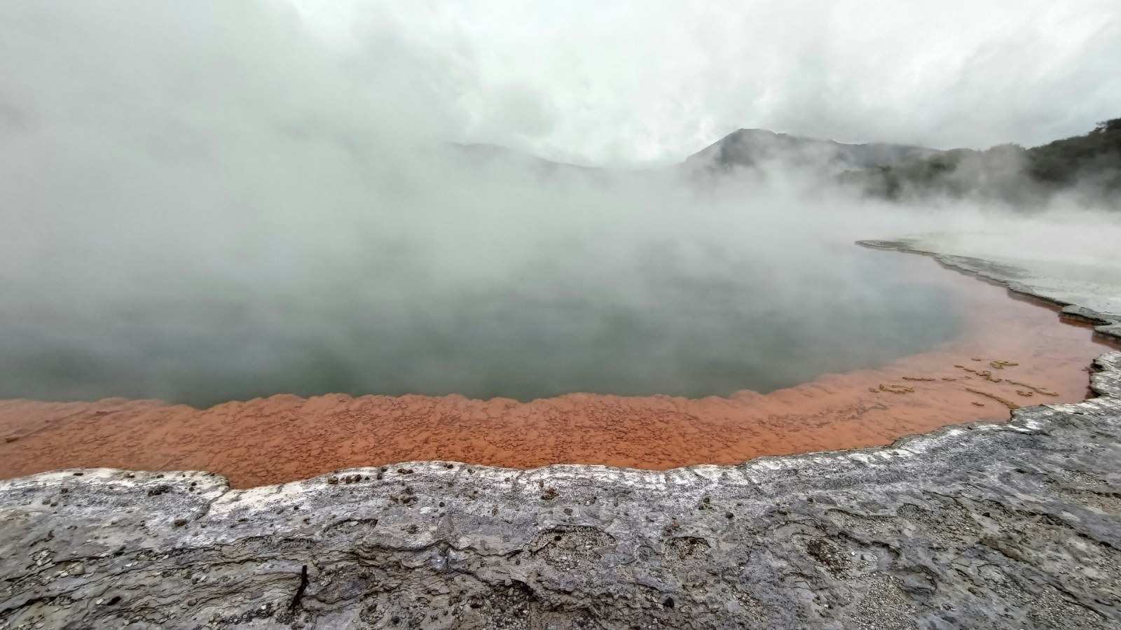 Aguas termales humeantes de colores turquesa y naranja en una zona geotérmica de Rotorua, Isla Norte de Nueva Zelanda