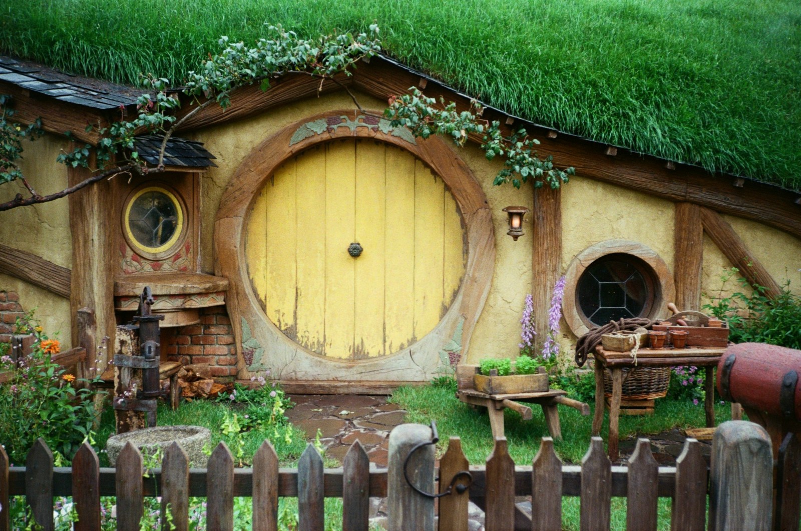 Puerta redonda amarilla de una casa hobbit en el set de rodaje de Hobbiton, Isla Norte de Nueva Zelanda, entre césped y flores