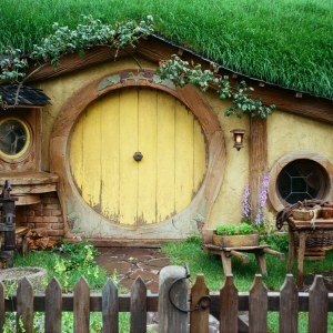 Puerta redonda amarilla de una casa hobbit en el set de rodaje de Hobbiton, Isla Norte de Nueva Zelanda, entre césped y flores