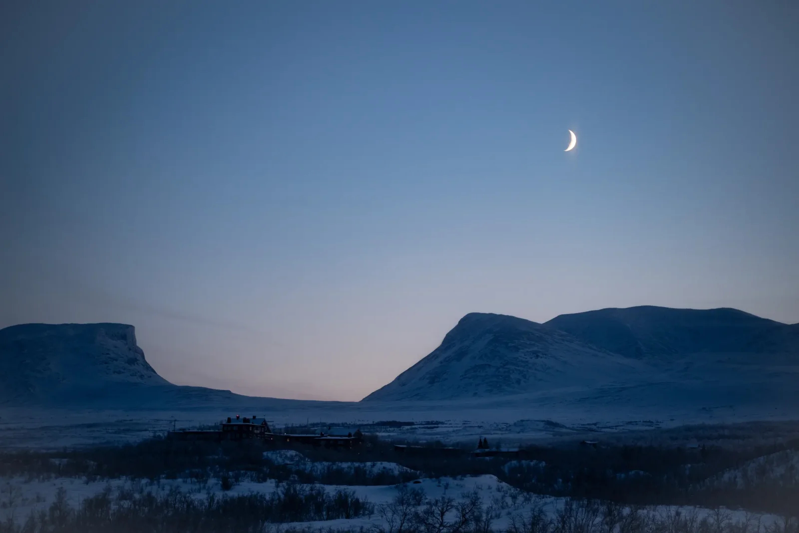 Luna creciente sobre las montañas nevadas de Abisko al atardecer de invierno