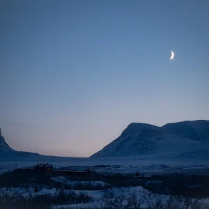 Luna creciente sobre las montañas nevadas de Abisko al atardecer de invierno