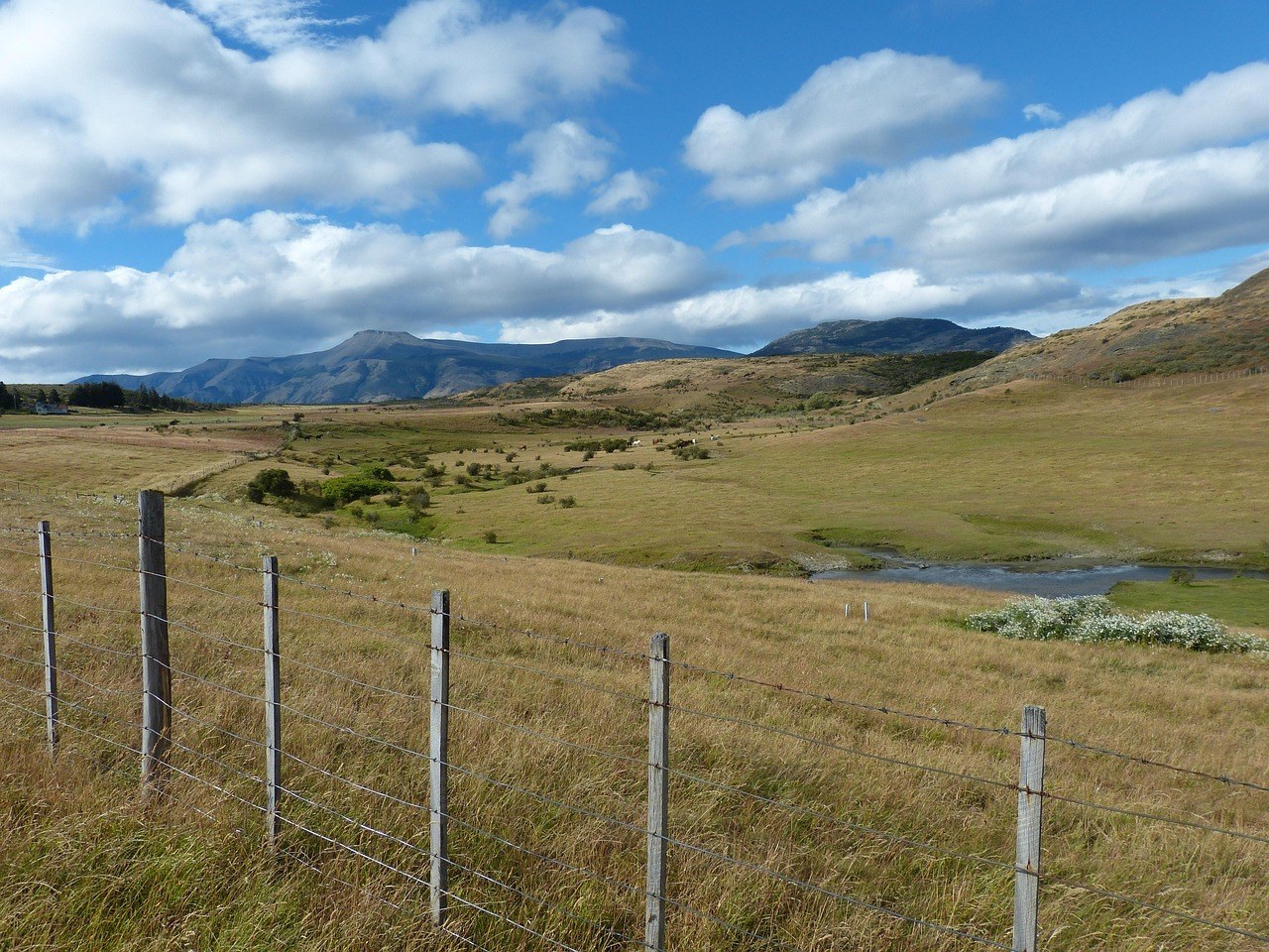 Paisaje rural de la Patagonia chilena, con una cerca de madera y montañas al fondo bajo un cielo nublado