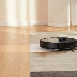 El Roborock S8 MaxV Ultra limpia un suelo de madera junto a una alfombra
